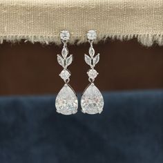 a pair of white diamond earrings hanging from a piece of cloth on top of a table