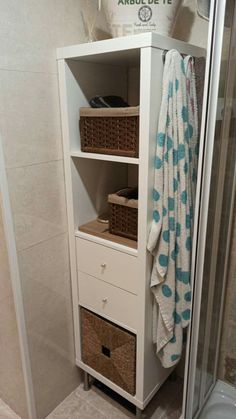 a white cabinet with baskets and towels on it next to a walk in shower stall