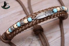 a braided leather bracelet with beads and an arrow charm on the end, sitting on a wooden surface