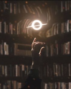 a person holding up a small object in front of a book shelf filled with books