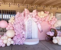 a pink and white balloon arch is decorated with balloons, flowers, and a baby carriage