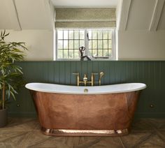 an old fashioned bathtub in a bathroom with green walls and wood flooring, next to a potted plant