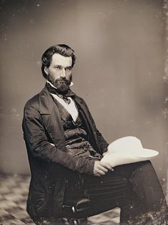 an old black and white photo of a man in a suit with a hat on his lap