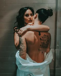 a man and woman embracing each other in the bathtub with tattoos on their back