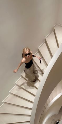 a woman in sunglasses is walking down a spiral stair case with her arms outstretched and legs spread out