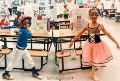 two young children are standing in front of desks with posters on the wall behind them