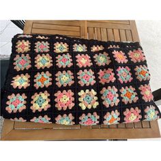 a crocheted granny blanket sitting on top of a wooden table next to a chair