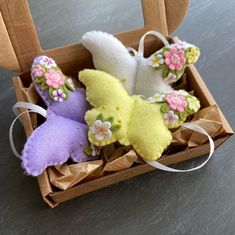 three stuffed animals are in a box on the table and one is yellow, purple, and white