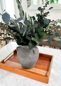 a gray vase with greenery in it sitting on a tray