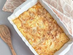 a casserole dish on a table with a wooden spoon next to it and an orange napkin