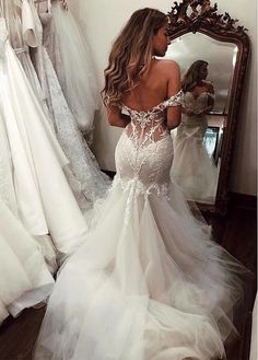 a woman standing in front of a mirror wearing a wedding dress with an open back