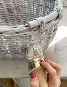 a woman holding a paintbrush in front of a wicker basket