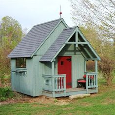 a small green house with a red door and porch in the grass next to trees