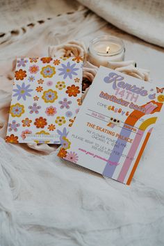 a couple of cards sitting on top of a bed next to a candle and some flowers