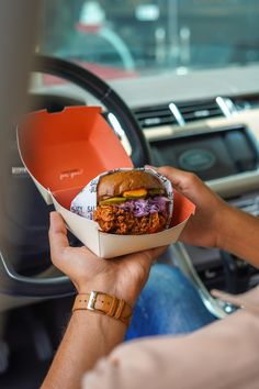 a person holding up a sandwich in their hand while sitting in the driver's seat