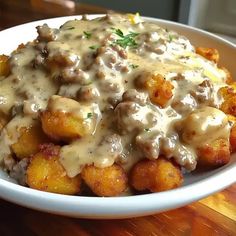 a white bowl filled with meat covered in gravy and potatoes on top of a wooden table