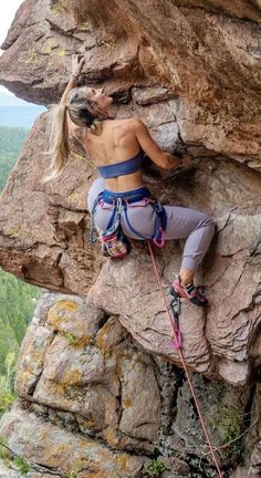 a woman climbing up the side of a mountain with her hands in her pockets and holding onto a rope