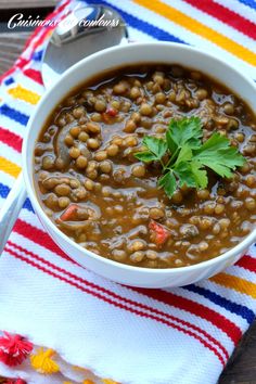 a white bowl filled with beans and garnished with parsley next to a spoon