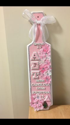 a pink and white tag with flowers on it hanging from the side of a wall