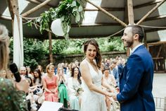 a bride and groom standing in front of an audience at a wedding ceremony, holding hands with each other