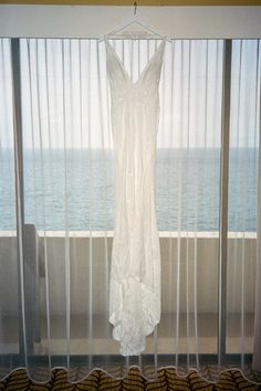 a dress hanging on a hanger in front of a window with sheer curtains overlooking the ocean