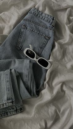 two pairs of jeans and sunglasses laying on a bed