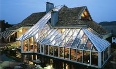 a house with a green roof that has glass walls and is lit up at night