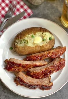 a plate with meat and baked potato on it next to a glass of beer in the background