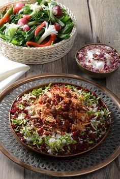 a salad in a bowl on a plate next to another dish with meat and vegetables