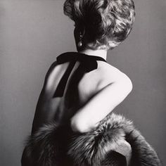 an old photo of a woman wearing a dress and fur stole around her neck, back to the camera