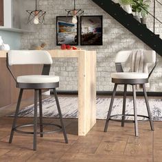 two white stools in front of a brick wall and wooden floor next to stairs