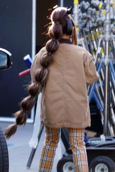 a woman with long hair standing in front of a car and talking on her cell phone