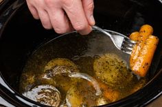 someone using a fork to stir up some food in the slow cooker with broth