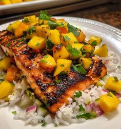 a white plate topped with fish and rice covered in pineapple salsa next to a tray of other food