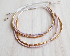 three bracelets with gold and white beads on a wooden surface, one has a beaded cord