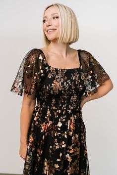 a woman with blonde hair wearing a black floral print dress and smiling at the camera