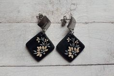 two square shaped black and white earrings with floral designs on them sitting on a wooden surface