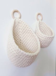 two crocheted baskets hanging from hooks on a white wall, one is empty and the other is closed