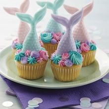 cupcakes decorated with pastel colors and mermaid tail decorations on a white plate