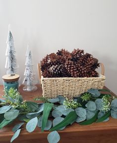 a basket filled with pine cones sitting on top of a table next to greenery