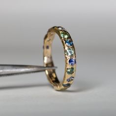 a gold ring with multi colored stones is being held by a pair of pliers