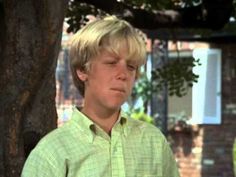 a young boy standing next to a tree