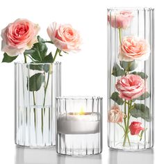 three clear vases with pink roses in them and a lit candle inside the one