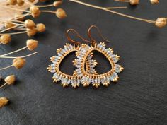 a pair of gold and white earrings sitting on top of a black surface next to dried flowers