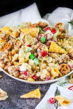 a white bowl filled with cereal salad next to crackers and candy caned candies