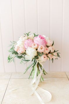 a bridal bouquet with pink and white flowers on a tile floor in front of a wall