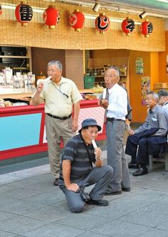 several people are sitting on benches in front of a food stand and one man is eating an ice cream cone