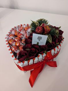 a heart - shaped box filled with chocolates and roses sits on a white table