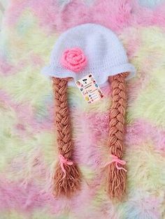 a knitted hat with two braids and a flower on the top is laying on a fuzzy surface