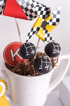 some cake pops are in a cup with race flags on top and dirt below them